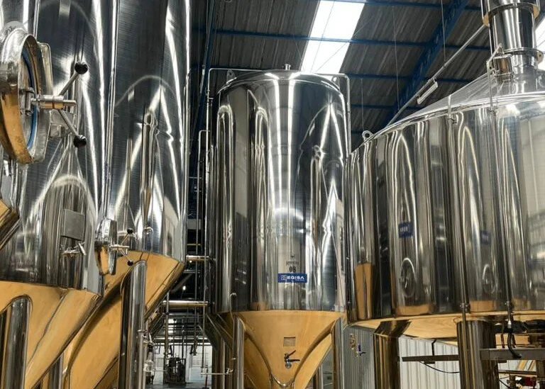 Tanques de fermentação da Ravache vistos de perto, com a estrutura do galpão ao fundo